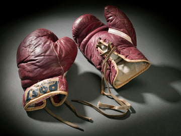 Vintage red boxing gloves with laces on a dark background.