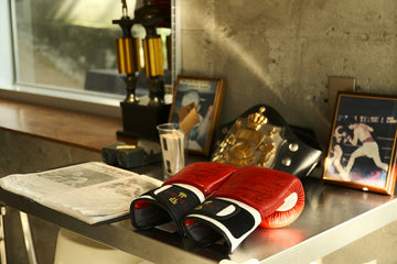 Red boxing gloves on a metal table with a championship belt and trophies
